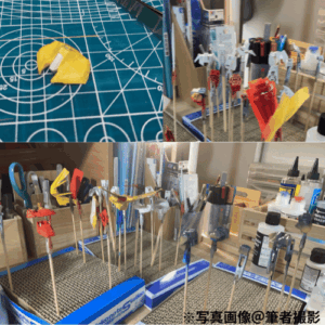SDEX Standardのエールストライクガンダムの製作風景写真です。塗装を行なっている模様で、マスキングテープで養生されているパーツや、塗装用の持ち手棒についたパーツを、塗装後に立てて自然乾燥させている画像です。