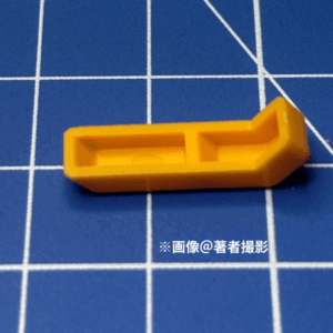 ガンプラのパーツ。跳ね返り実験に用いたピース。素材はABS、大きい方。形状は細長く。脛の部分と推察。黄色