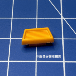 ガンプラのパーツ。跳ね返り実験に用いたピース。素材はABS、中間の大きさ。形状は台形のファンの部分。黄色。
