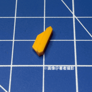 ガンプラのパーツ。跳ね返り実験に用いたピース。素材はABS、小さい方。形状は台形。おそらく脚部のスラスター。黄色