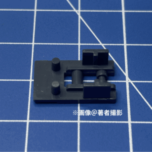 ガンプラのパーツ。跳ね返り実験に用いたピース。素材はPS、大きい方。形状は平な四角にはめ込み部分がる。濃いグレー