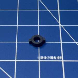 ガンプラのパーツ。跳ね返り実験に用いたピース。素材はP E、小さい方。形状は円形の0度と180度部分に突起がある。濃いグレー